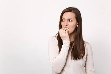 Portrait of preoccupied shocked young woman in light clothes looking aside, gnawing nails isolated on white wall background in studio. People sincere emotions, lifestyle concept. Mock up copy space.