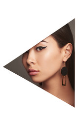 Cropped side geometric portrait of lady with fresh makeup and black flicks. The young woman is wearing long earrings in view of geometric figure, looking at camera behind triangle-shaped foreground.