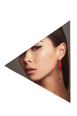 Cropped side geometric portrait of Asian woman with black flicks, tilting her head. The girl is wearing long earrings in view of geometric figure, looking at camera behind triangle-shaped foreground.