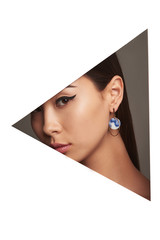 Cropped side geometric portrait of Asian woman with black flicks, tilting her head. The lady is wearing long earrings with blue smoky pattern, looking at camera behind triangle-shaped foreground.