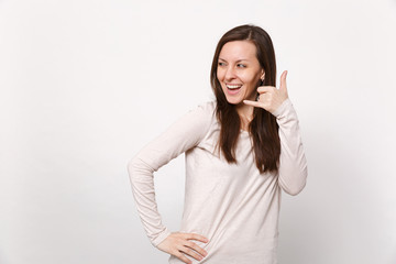 Cheerful young woman in light clothes looking aside, doing phone gesture like says call me back isolated on white background in studio. People sincere emotions, lifestyle concept. Mock up copy space.