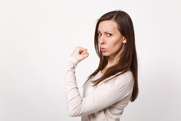 Portrait of strong serious attractive young woman in light clothes showing biceps, muscles isolated on white wall background in studio. People sincere emotions, lifestyle concept. Mock up copy space.