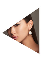 Cropped half-turn geometric portrait of girl woman with dark hair. The lady is wearing dangle earrings with smoky beige pendant, tilting head and looking at camera behind triangle-shaped foreground.