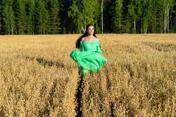 Naklejka na ściany i meble beautiful young woman in green dress runs across the wheat field