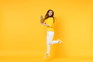 Fototapeta na wymiar Smiling young woman in casual clothes jumping, hold fresh ripe pineapple fruit isolated on yellow orange wall background in studio. People vivid lifestyle, relax vacation concept. Mock up copy space.