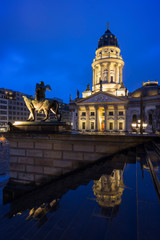 Fototapeta premium Lit Neue Kirche (Deutscher Dom, German Church or German Cathedral) and a statue in front of the Konzerthaus Berlin (Berlin Concert Hall) at the Gendarmenmarkt Square in Berlin, Germany, at dusk.