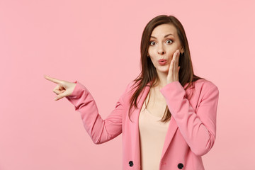 Amazed young woman wearing jacket putting hand on cheek, pointing index finger aside isolated on...