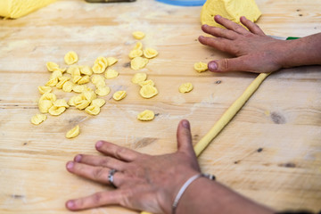 Hands of women preparing the traditional Italian pasta orecchiette, in the Bari region.Hands of...
