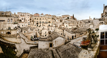 Obraz premium Panoramic view of Matera (Sassi di Matera) with its steep ancient stone streets, European Capital of Culture 2019, with clouds, at southern Italy, waiting to welcome tourists.