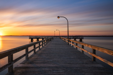 Fototapeta na wymiar Warm golden light on an empty fishing pier at sunset. Soft pastel clouds streaking across the sky.