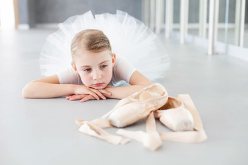 Little ballerina is looking at pointe shoes in ballet class. Cute child girl is dreaming and lying...