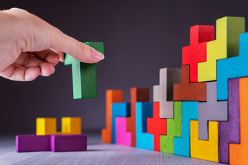 Geometric shapes on a wooden background. Hand sets the element of the puzzle.