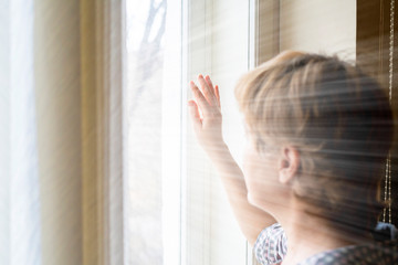 woman pushes the blinds and looks out the window