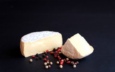 Camembert cheese with some diverse type of pepper in foreground. Black background. Copy space.