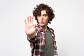 Fototapeta premium Portrait of concerned young man in casual clothes looking camera, showing stop gesture with palm isolated on white background in studio. People sincere emotions, lifestyle concept. Mock up copy space.