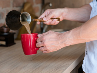 Morning. Coffee making time. Man leisure and lifestyle. Hands with jezve pouring latte into red cup.