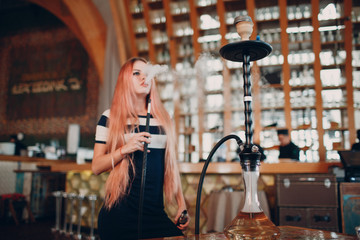 Fototapeta na wymiar Young beautiful female smoking hookah. Smoke shisha hookah in cafe concept.