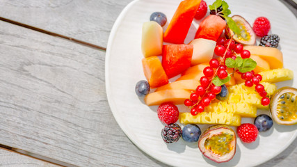 Bowl of healthy fresh fruit salad on wooden background. Top view