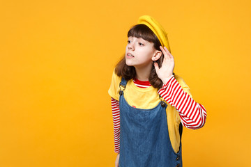Curious girl teenager in french beret, denim sundress looking aside, eavesdrop with hearing gesture...