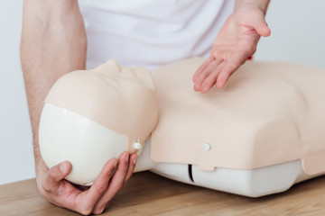 cropped view of man holding dummy and gesturing while practicing cpr during first aid training