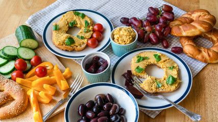 Sunday morning vegan breakfast with colorful vegetables, homemade bagels and hummus with homegrown basil, olives and grapes. Healthy organic food and lifestyle concept.