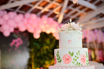 white birthday cake decorated with pink roses and balloons in the background