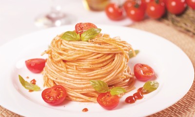 Spaghetti pasta with cherry tomatoes and basil leaves on white plate