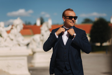 Fashion man in stylish blue suit and tie bow. He also wears sunglasses and and luxury watch