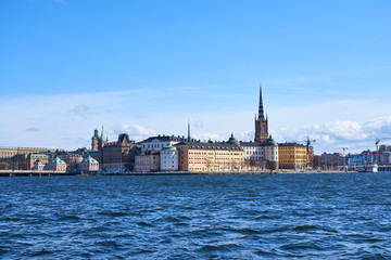 Fototapeta na wymiar Old city of Stockholm with waves on blue water under the blue cloudy sky in sunshine.