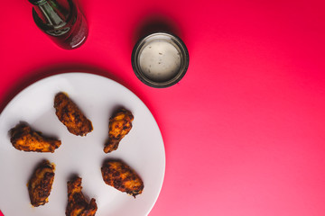 Chicken wings, dipping sauce and beer on pink background.