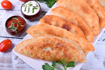 Golden Chebureki on a white plate. Sauces, vegetables and greenery around