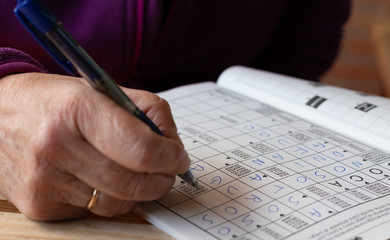 Hand of senior person doing crosswords puzzle's in a notebook. Leisure and free time.