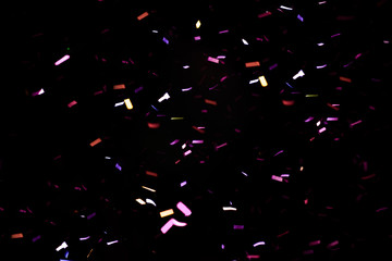 Thousands of confetti fired on air during a festival at night. Image ideal for backgrounds. Multicolor are the confetti in the picture. The sky as background is black. Purple/pink tonality