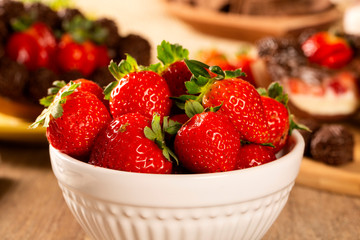 several strawberries in a white pot on a wooden table with easter egg background.