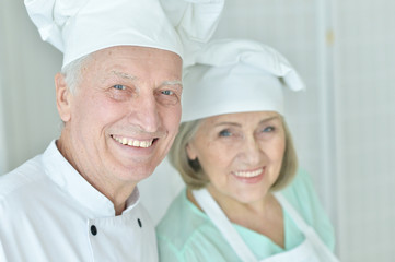 Portrait of couple of smiling senior chefs at kitchen