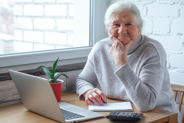 An old woman is sitting at the table in front of laptop.