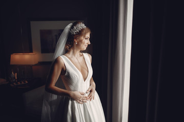 Beautiful bride standing near window. The girl in a white wedding dress