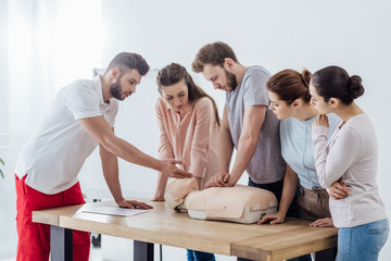 group of people with handsome instructor performing cpr on dummy during first aid training