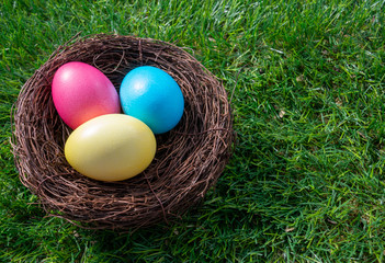 Fototapeta premium Three painted easter eggs in a nest on green grass