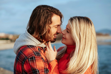 Fototapeta premium Young couple on the beach hugging and looking at each other with love. Holidays at sea on vacation. Portrait at sunset.