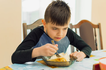 boy of European appearance sits at the table and has breakfast, he eats dairy products with a fork...