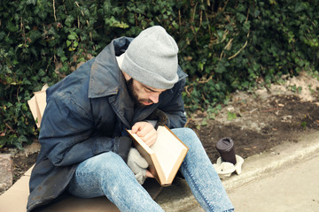 Poor homeless man with book on street in city