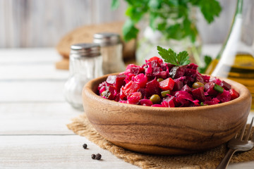 Traditional russian salad vinaigrette with boiled vegetables, pickled cucumbers and sauerkraut in bowl on white wooden table. Selective focus.