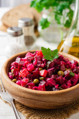 Traditional russian salad vinaigrette with boiled vegetables, pickled cucumbers and sauerkraut in bowl on white wooden table. Selective focus.