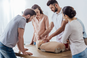 group of concentrated people with cpr dummy during first aid training class