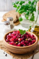 Traditional russian salad vinaigrette with boiled vegetables, pickled cucumbers and sauerkraut in bowl on white wooden table. Selective focus.