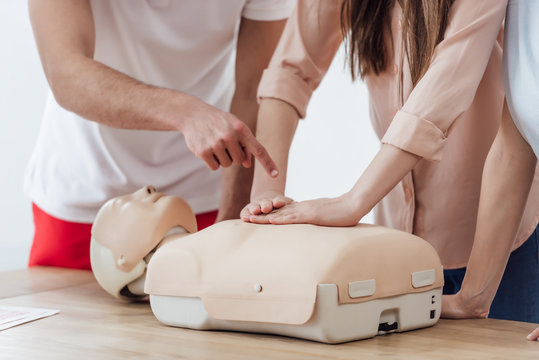 partial view of woman performing chest compression on dummy during cpr training class while instructor pointing with finger