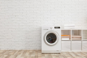 Modern washing machine near brick wall in laundry room interior, space for text - obrazy, fototapety, plakaty