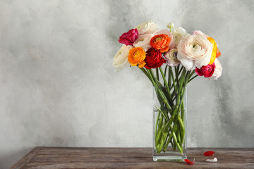 Vase with beautiful spring ranunculus flowers on wooden table, space for text