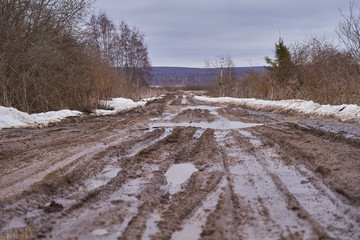 Obraz premium Broken dirt road with puddles in early spring